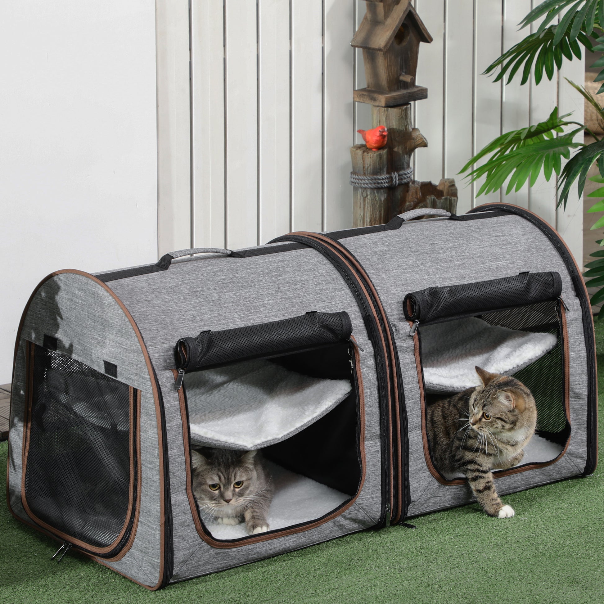 Gray pet carrier with two cats inside on a green surface.